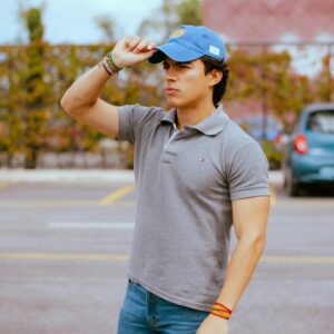 Young man in casual outfit and cap standing outdoors, conveying confidence.