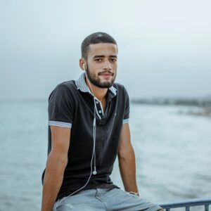 A young man in a polo shirt and earphones sits by the sea in Nabeul, Tunisia.